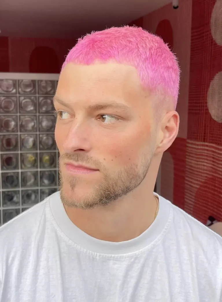 Man met kort, felroze haar geverfd in de stijl van Colorbar Twiggy James, kijkt opzij in een modern ingerichte ruimte.