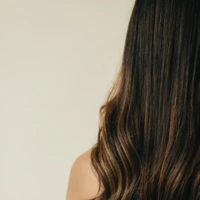 Achteraanzicht van lang, glanzend golvend bruin haar van een brunette tegen een neutrale achtergrond.