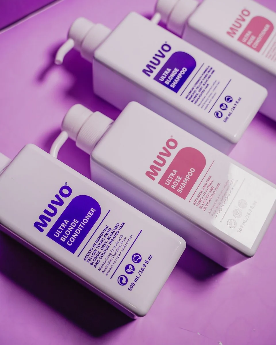 Vier flessen MUVO-haarverzorgingsproducten, waaronder de Ultra Rose Shampoo, liggen naast elkaar op een paarse ondergrond.